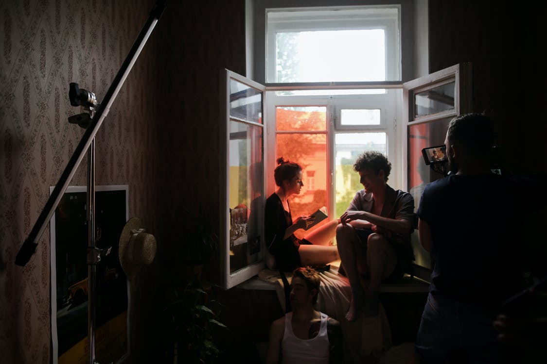 Filmmaker shooting a documentary about young couple in a dark room sitting by a window