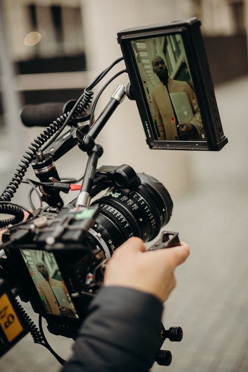 A person holding a camera filming a guy in brown coat holding a MacBook laptop