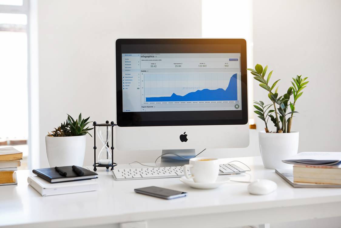 insurance graph on mac computer on a white table with coffee plants keyboard notebooks and books